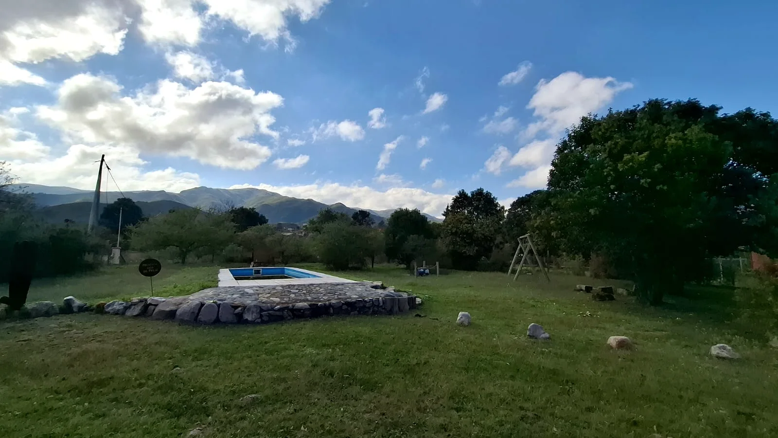Parque del refugio con la pileta, una hamaca de madera y las sierras de fondo